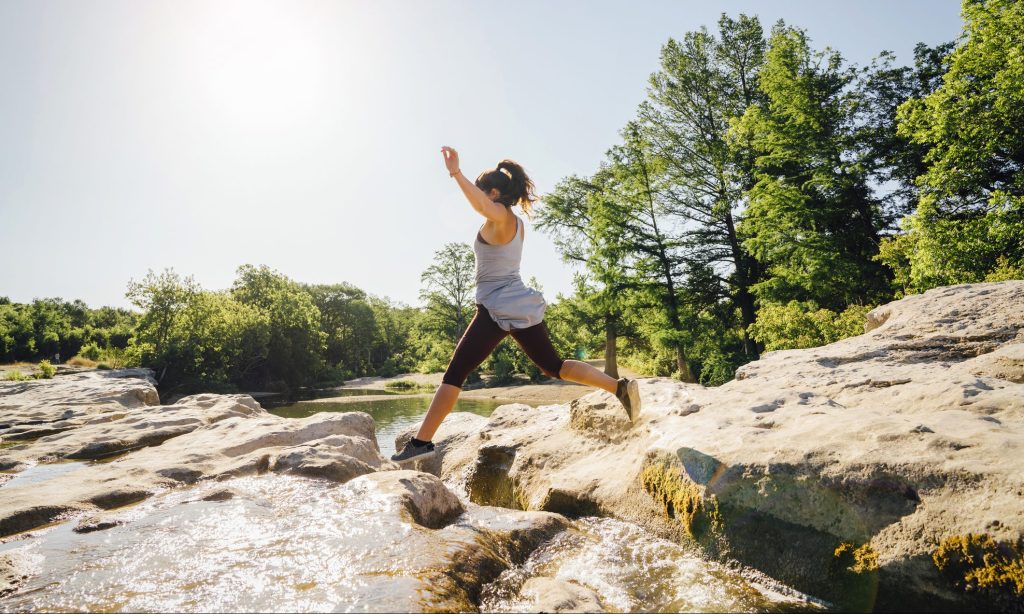 Caucasian woman jumping on rocks near river