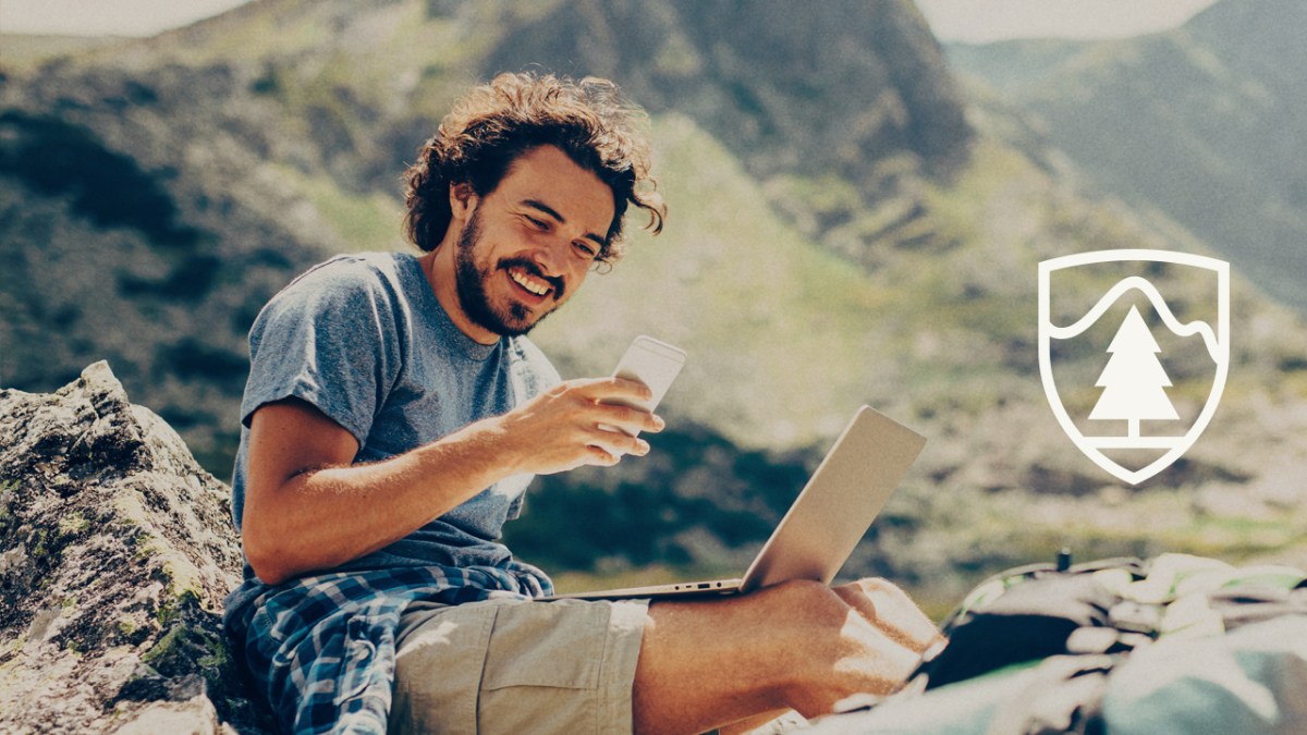 A thermos in the hands of a traveler. A man in tourist clothes with a thermos of coffee or tea in his hand against the background of nature, close-up. Travel and camping concept. Warming drink