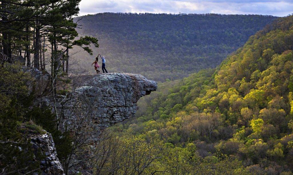 A couple dances with joy while standing on Hawksbill Crag at Whitaker Point in the Ozark Mountains of Northwest Arkansas at sunrise.