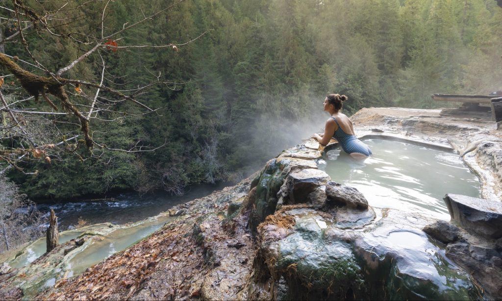 Woman with blue swimsuit relaxing in a hot pool in autumn, Umpqua Hot Springs, Douglas county, Oregon, United States.