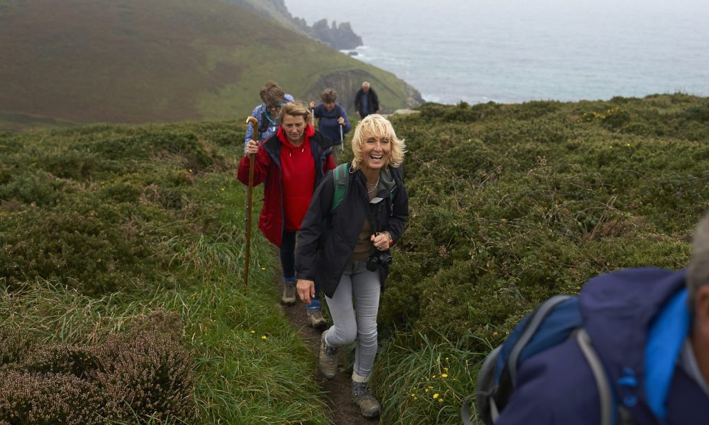A woman laughs as part of a senior ramblers group whilst hiking along an Atlantic coastal path.