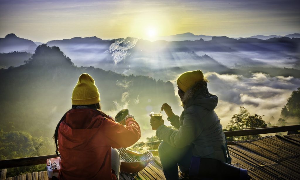 Group of normadic traveler in motion of enjoy takes food instant breakfast on the peak of mountain in the morning, enjoy having meal together in the mist foggy flowing in between the mountains hills