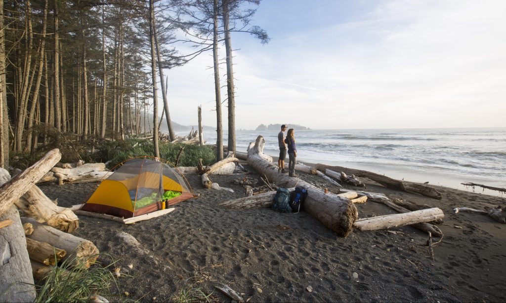 A couple watching sunset while backpacking along the coast in the Olympic National Park.